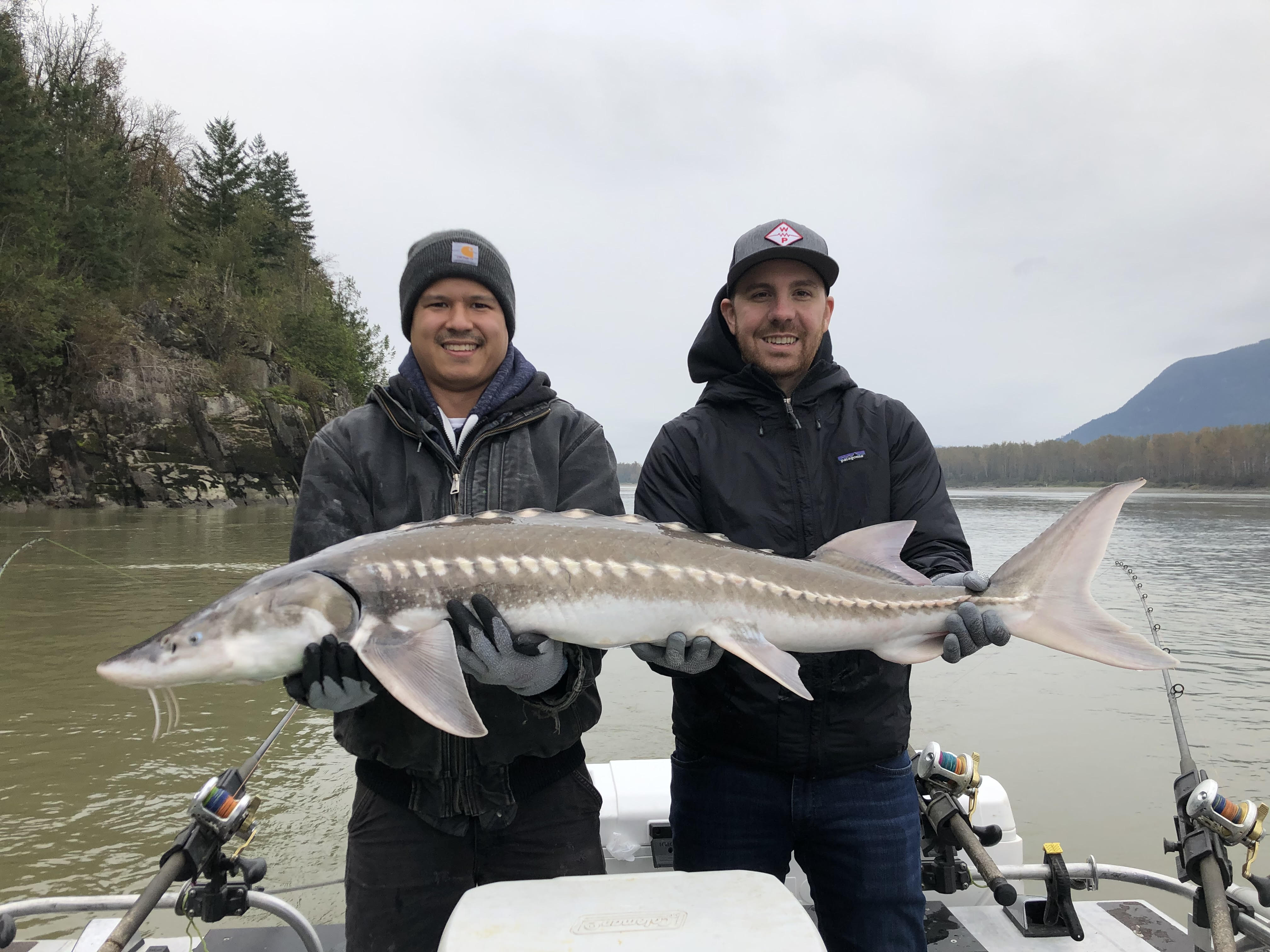 2 men holding a sturgeon on a boat